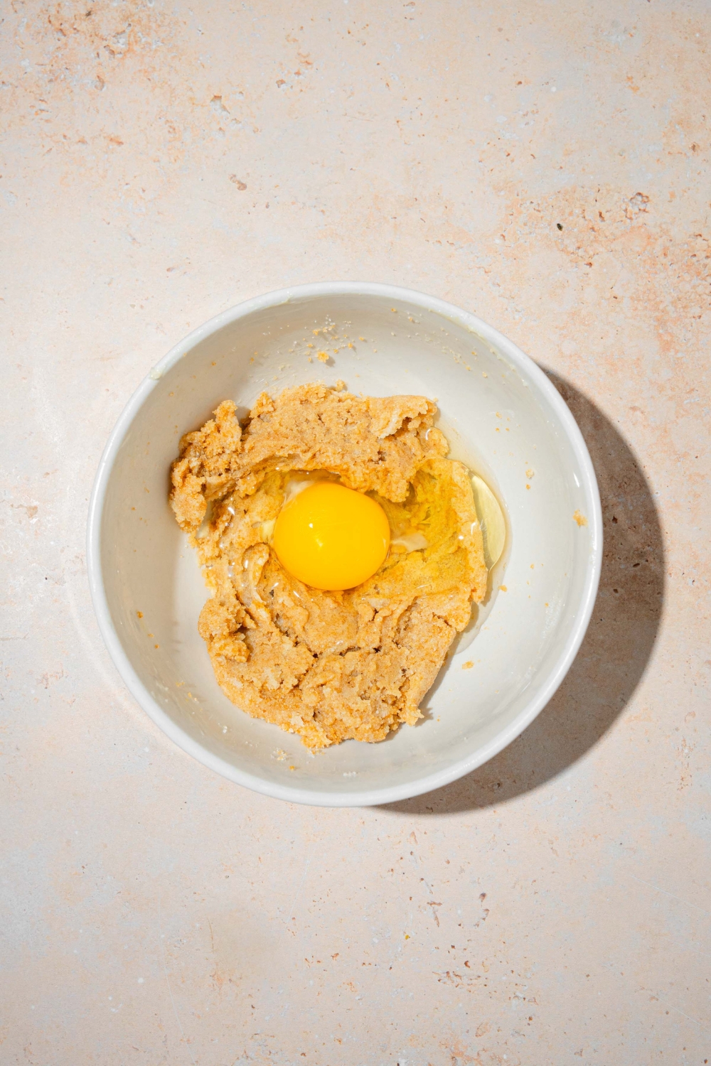 A large white bowl with a wet ingredient mixture an an egg to make chocolate chip cookie fry dough. The bowl is on a tan counter.