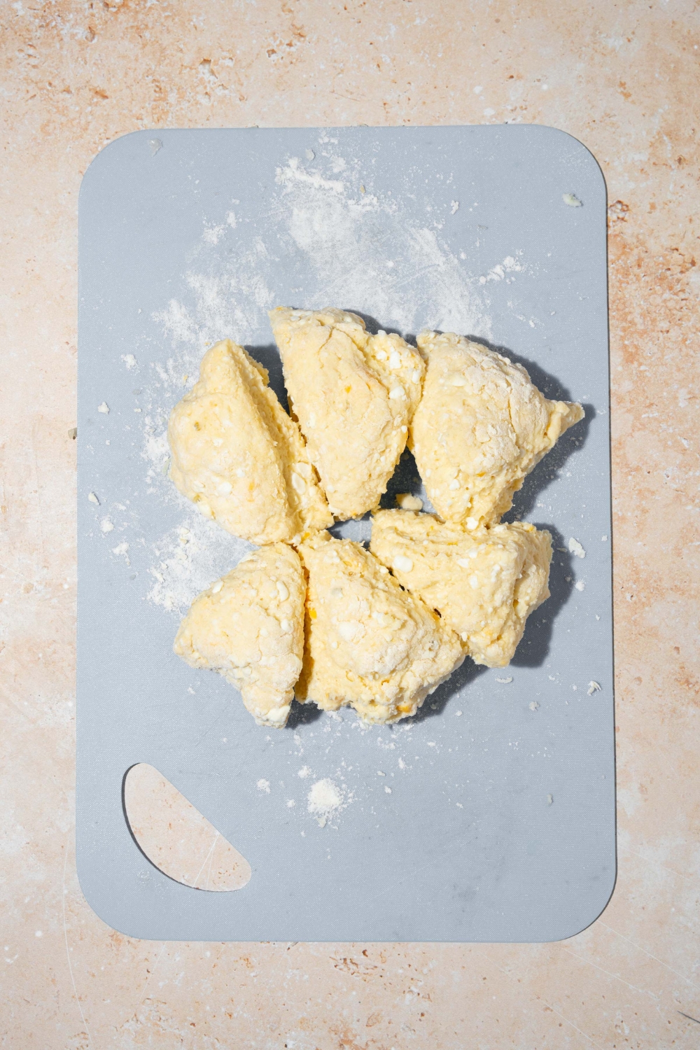 A cutting board with cottage cheese breadstick dough sliced into equal pieces. The cutting board is on a tan counter.