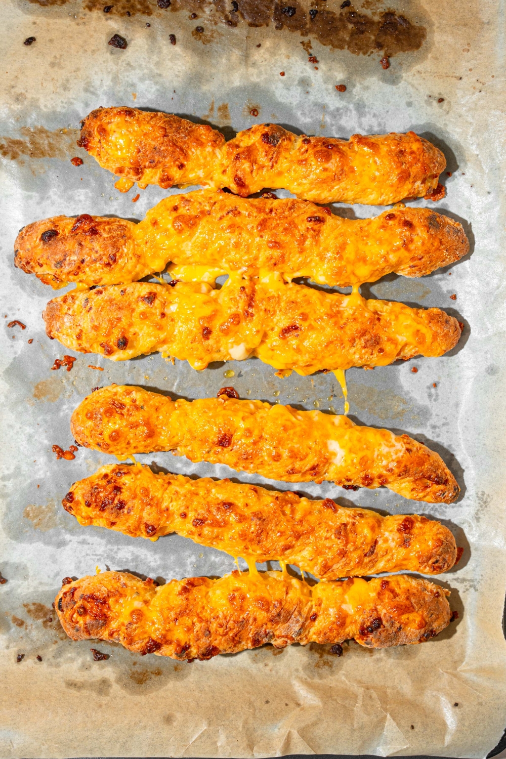 A baking sheet lined with parchment paper with several baked cottage cheese breadsticks. The sheet is on a tan counter.
