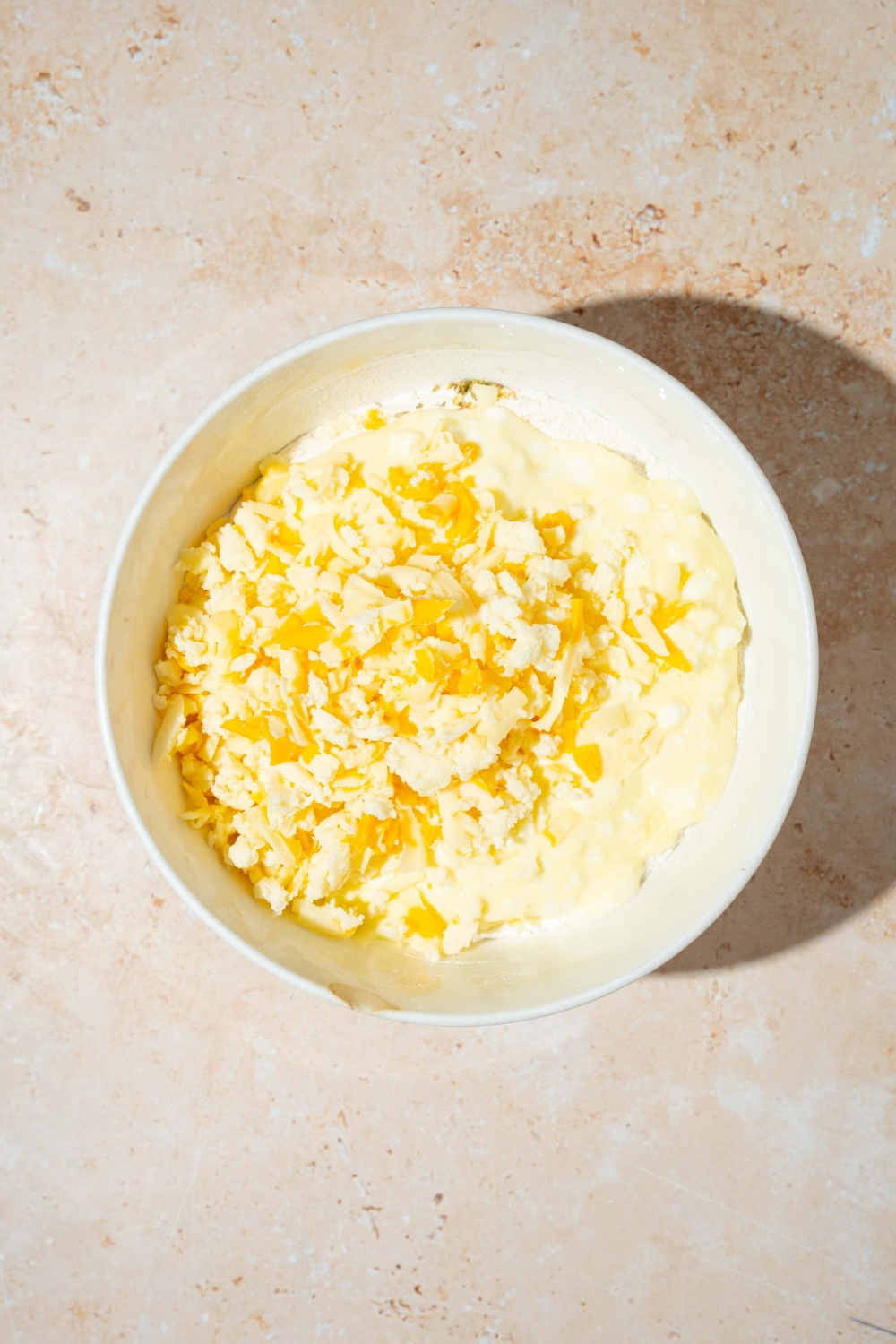 A large white bowl with ingredients to make cottage cheese breadstick dough including flour, cottage cheese, and shredded cheese. The bowl is on a tan counter.