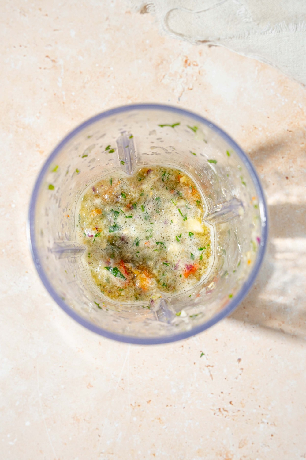 A food processor blender with blended ingredients to make crack sauce including shallot, red onion, bird's eye chilis, lime juice, and more.