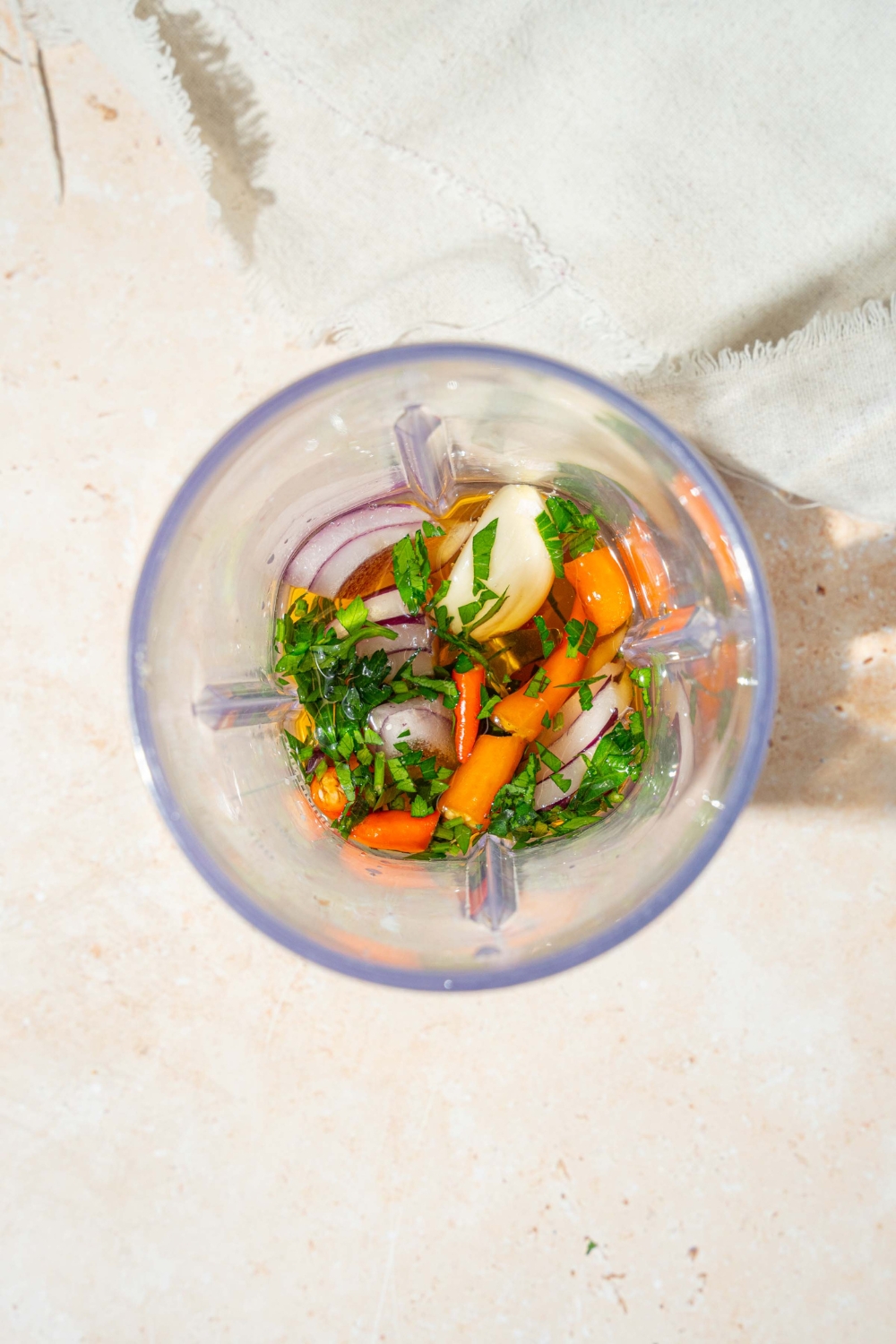 A food processor blender with ingredients to make crack sauce including shallot, red onion, bird's eye chilis, lime juice, and more.