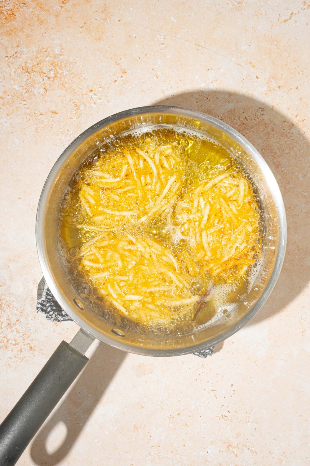 A pot of parmesan hashbrowns frying in oil. The pot is on a tan counter.