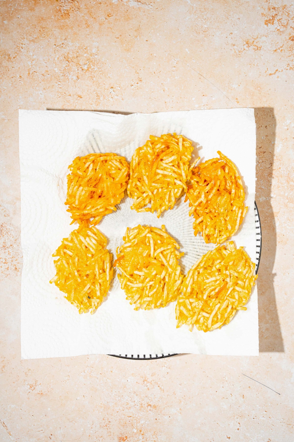 A plate lined with a paper towel with fried parmesan hashbrowns. The plate is on a tan counter.