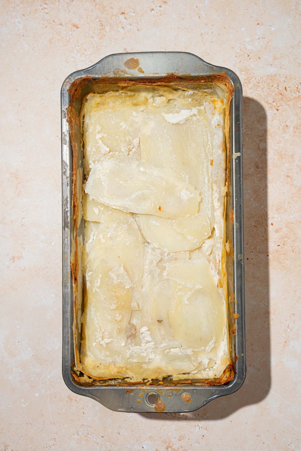 A loaf pan with baked potato pave. The pan is on a tan counter.
