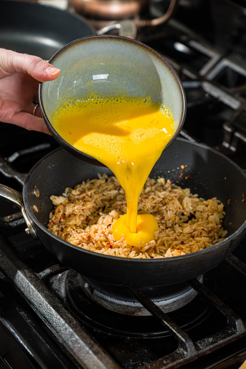 A skillet with crispy rice and a bowl of whisked egg being poured into the skillet.
