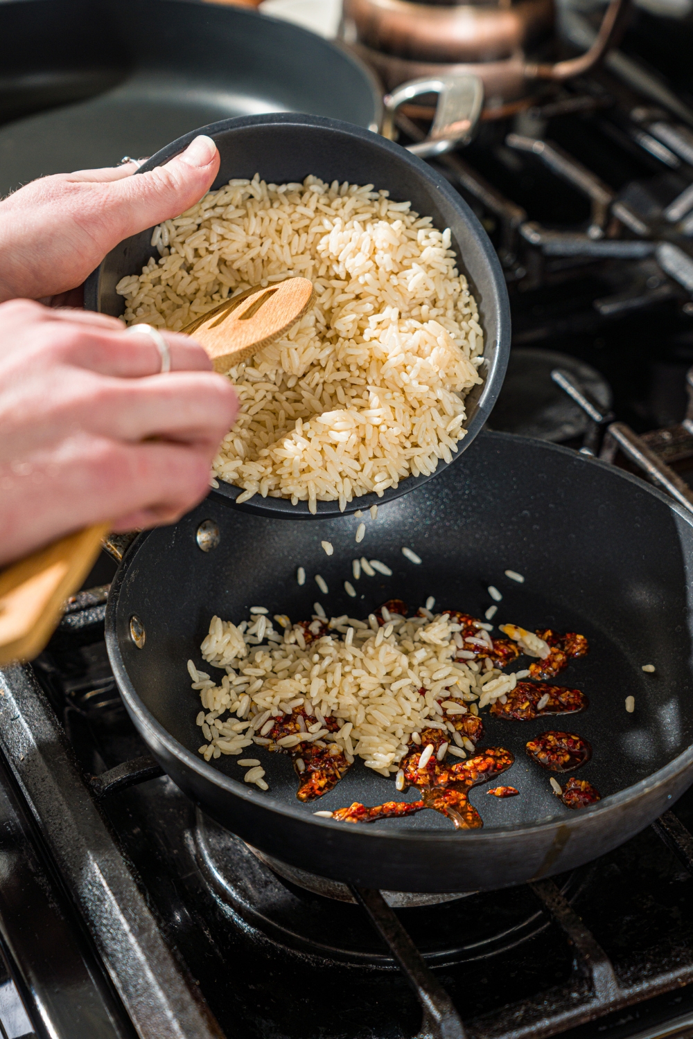 A bowl of rice being added to a skillet with chili crunch oil.