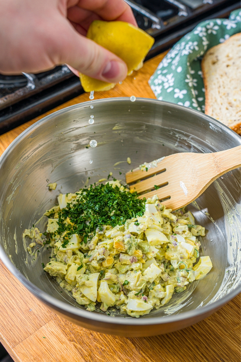 A large bowl with lemon being squeezed into a pickle egg salad mixture topped with fresh parsley. The bowl is on a wooden counter.