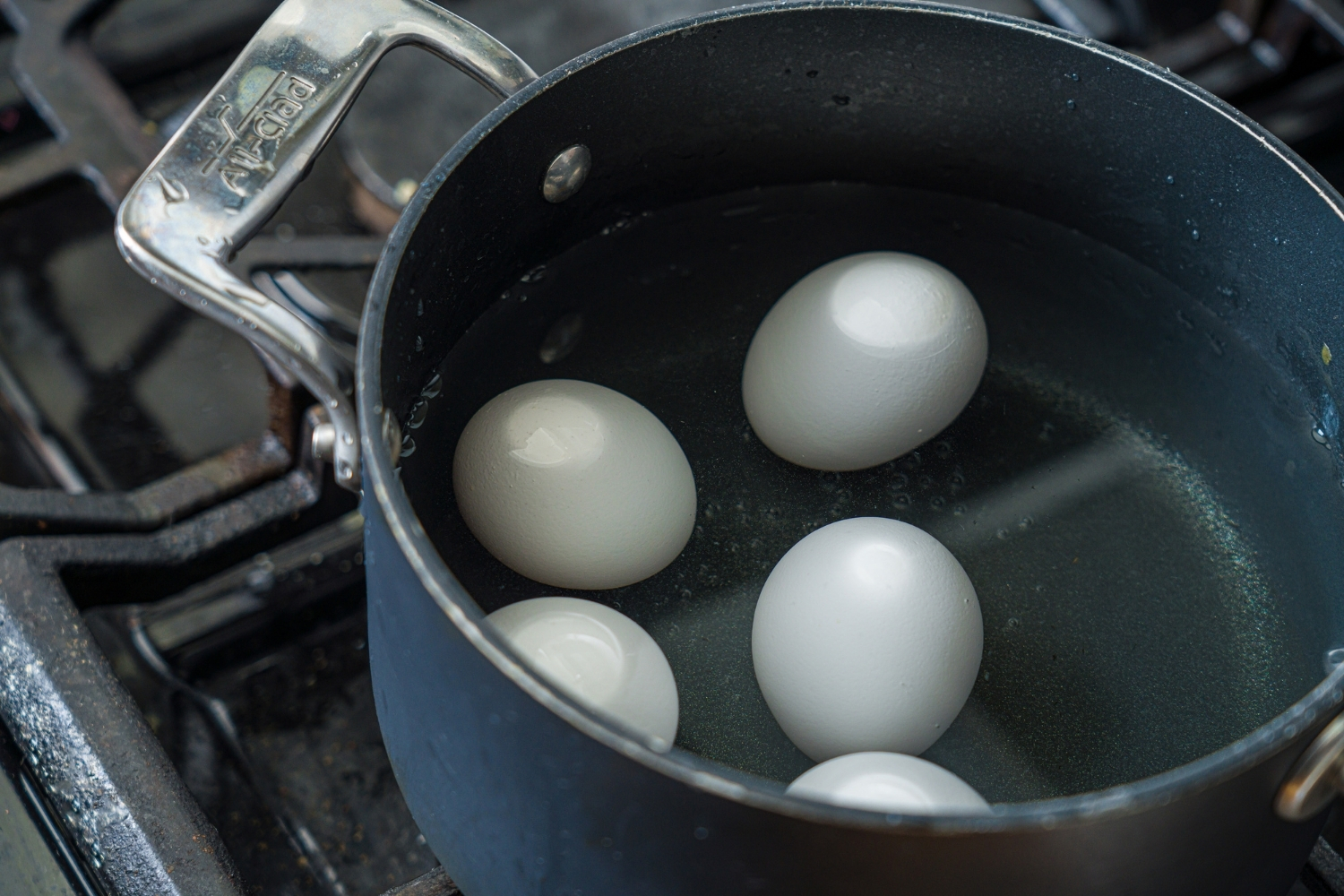A pot with several eggs in hot water. The pot is on a stove.