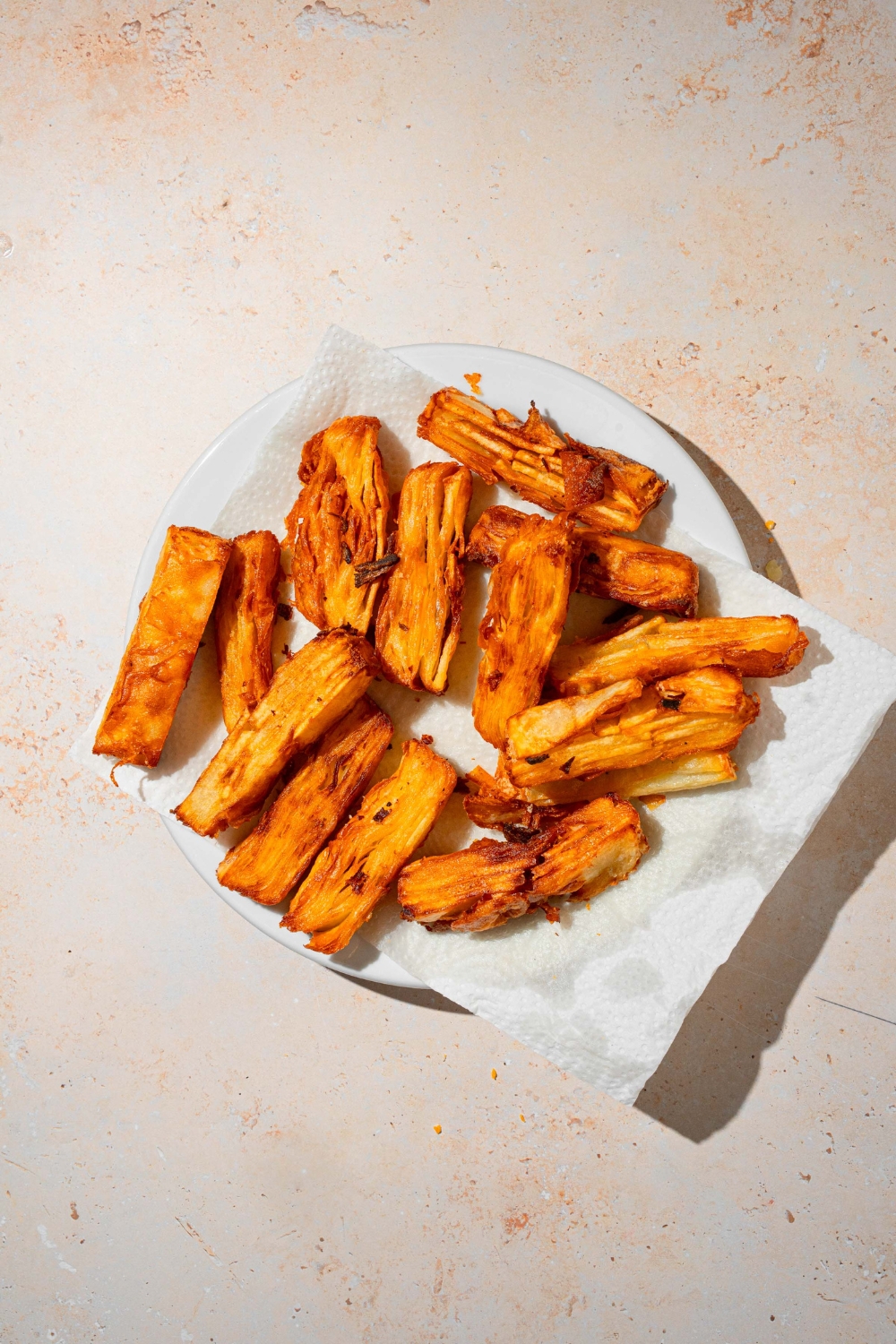A white plate lined with parchment paper with fried potato pave pieces. The plate is on a tan counter.