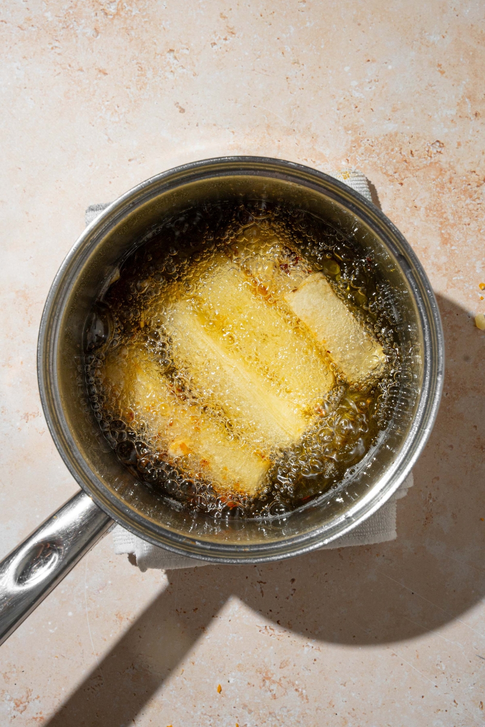 A stock pot with potato pave pieces frying in oil. The pot is on a tan counter.