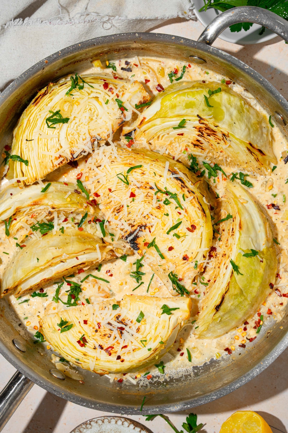 A skillet with baked garlic parmesan melting cabbage garnished with fresh parsley, red pepper flakes, and shredded parmesan cheese.