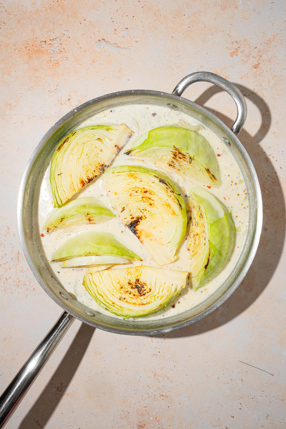 A skillet with sautéed cabbage wedges in a garlic parmesan cream sauce. The skillet is on a tan counter.