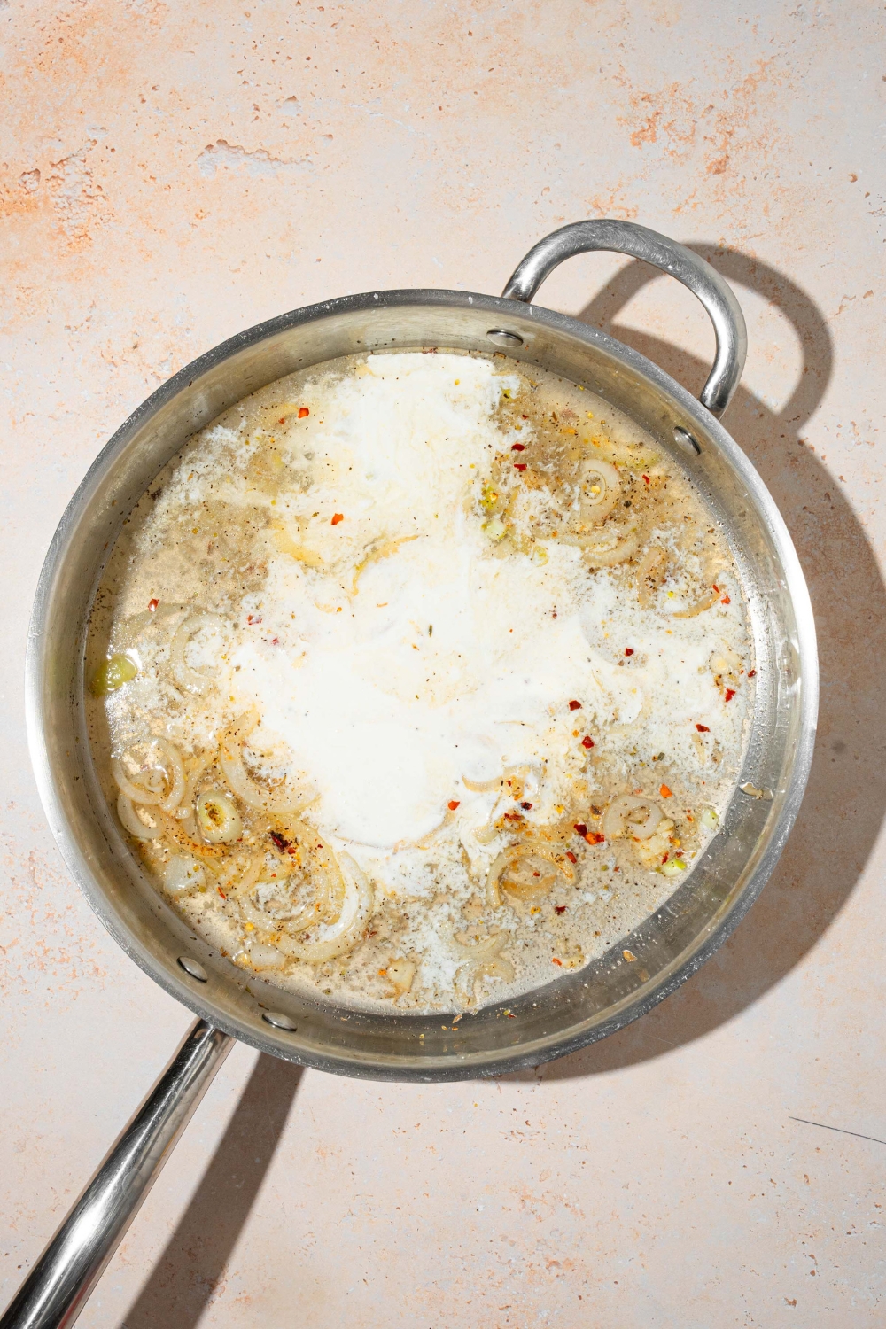 A skillet with garlic parmesan cream sauce mixture including sautéed onion, garlic, chicken broth, heavy cream, and seasonings. The skillet is on a tan counter.