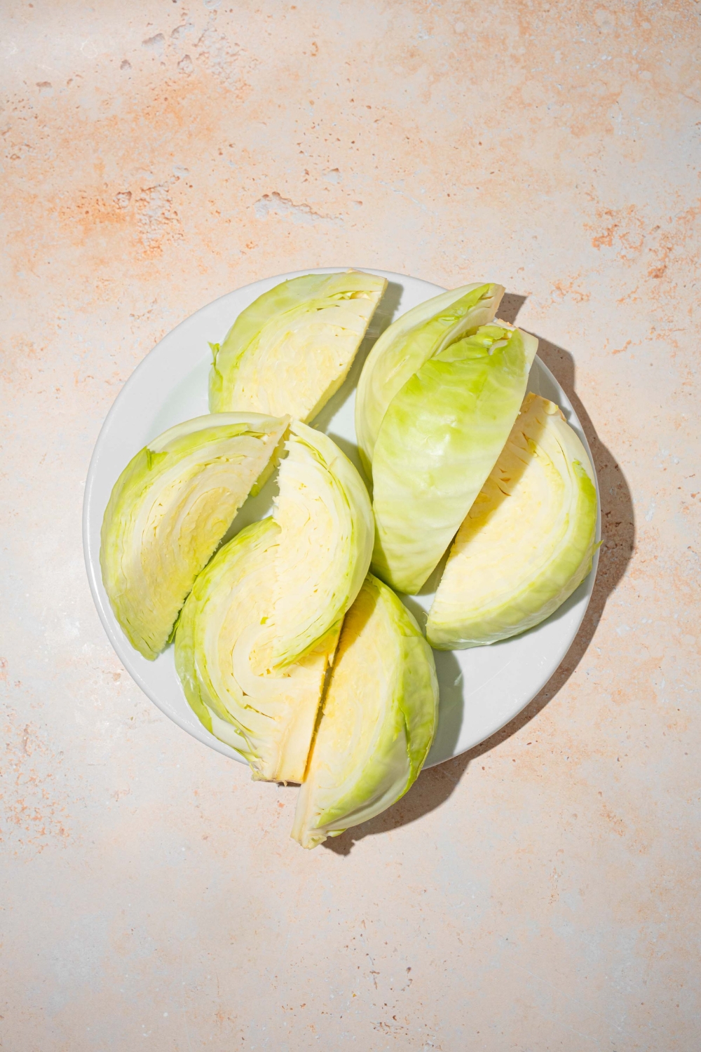 A white plate with cabbage sliced into wedges. The plate is on a tan counter.