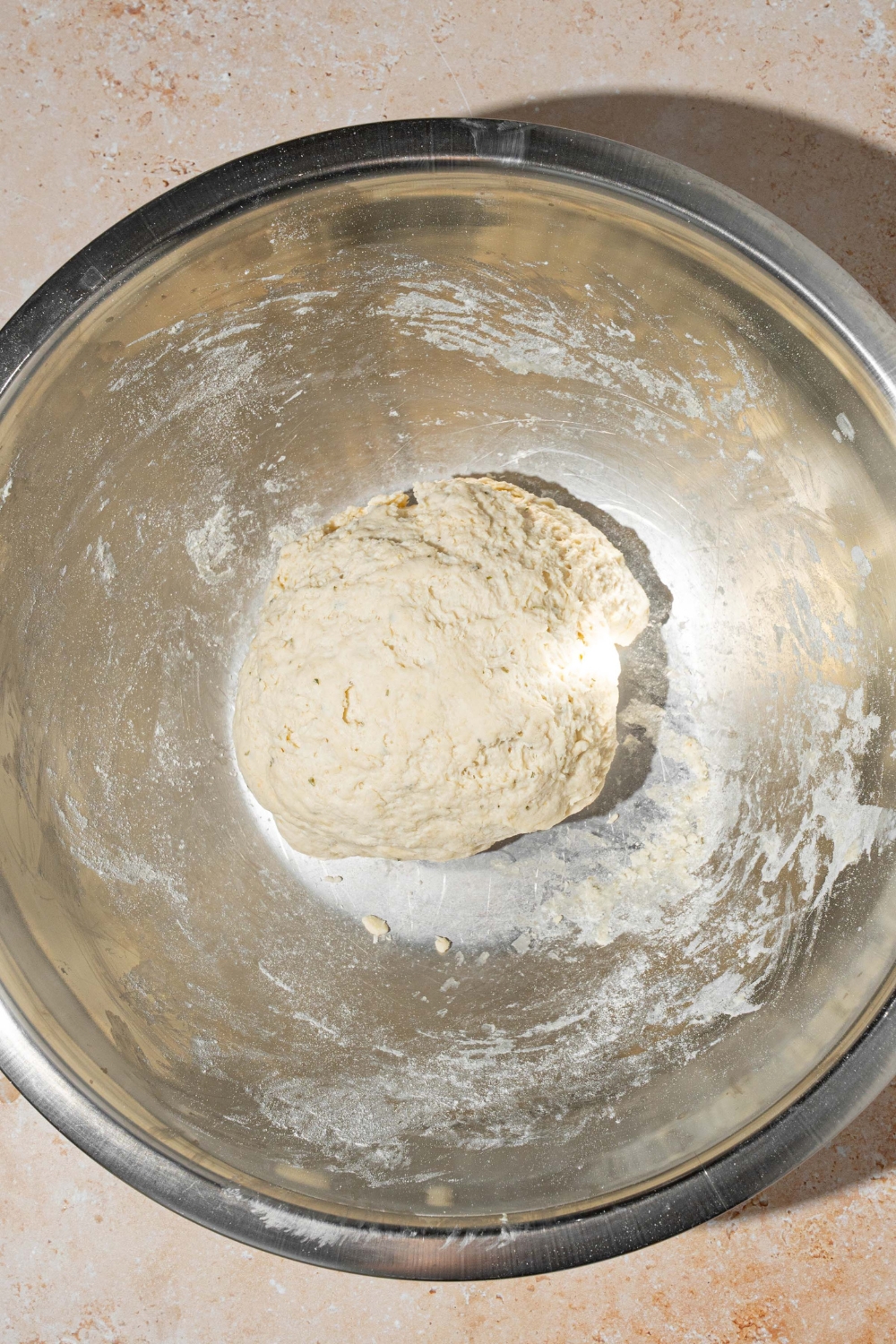 A large bowl with a kneaded dough ball. The bowl is on a tan counter.