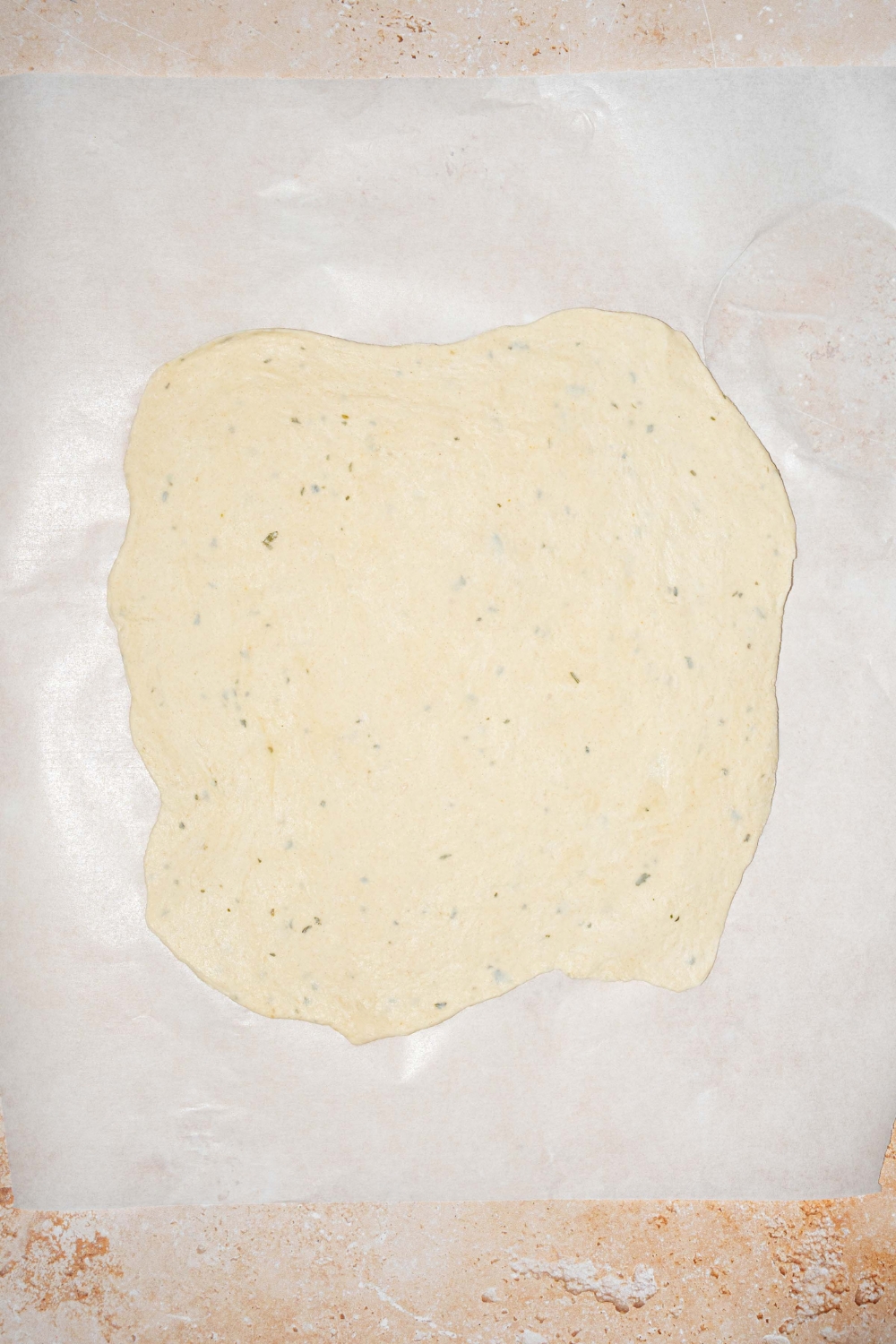A piece of parchment paper with dough rolled out into a rectangle shape.