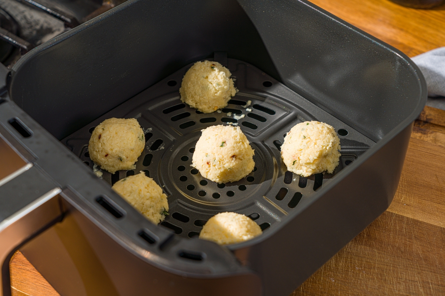 Several parmesan cheese balls in an air fryer. The air fryer is on a wooden board.