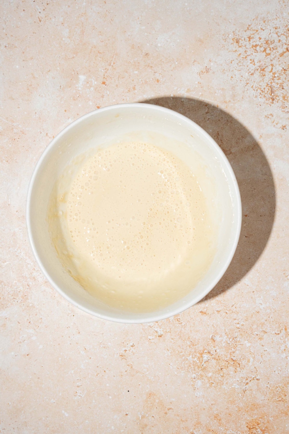 A large white bowl with vanilla cream cheese foam. The bowl is on a tan counter.
