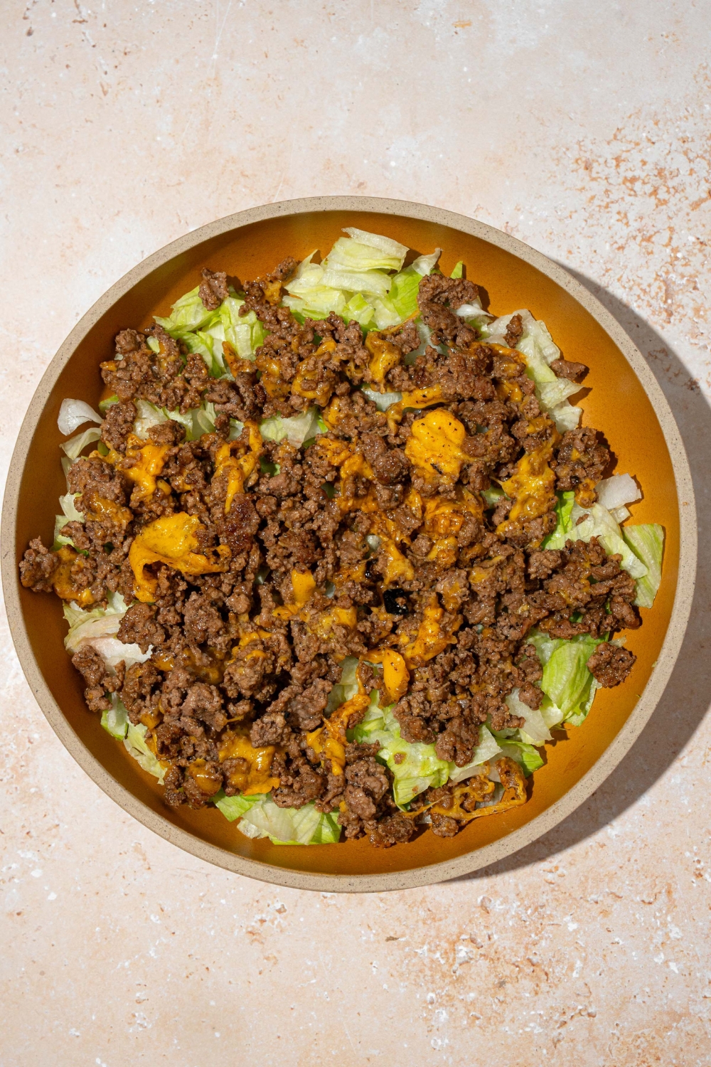 An orange plate with shredded lettuce and ground burger meat with melted cheese. The plate is on a tan counter.