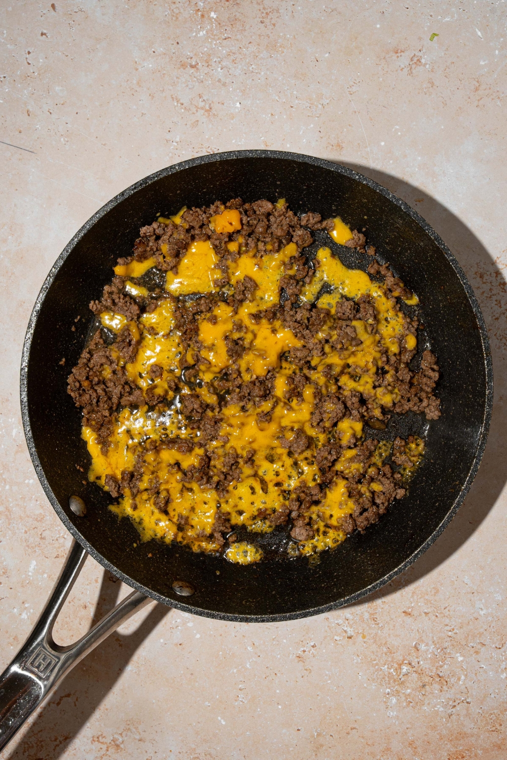 A skillet with a seasoned ground beef mixture with melted cheese. The skillet is on tan counter.