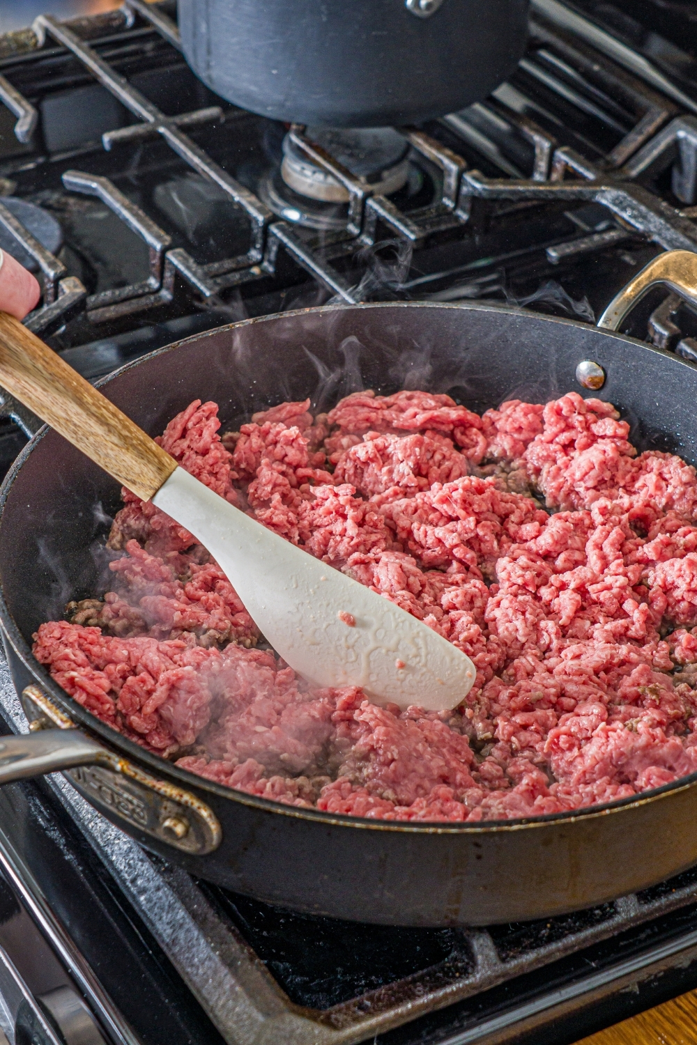 An oven with a skillet cooking ground beef. A spatula is breaking up the beef.