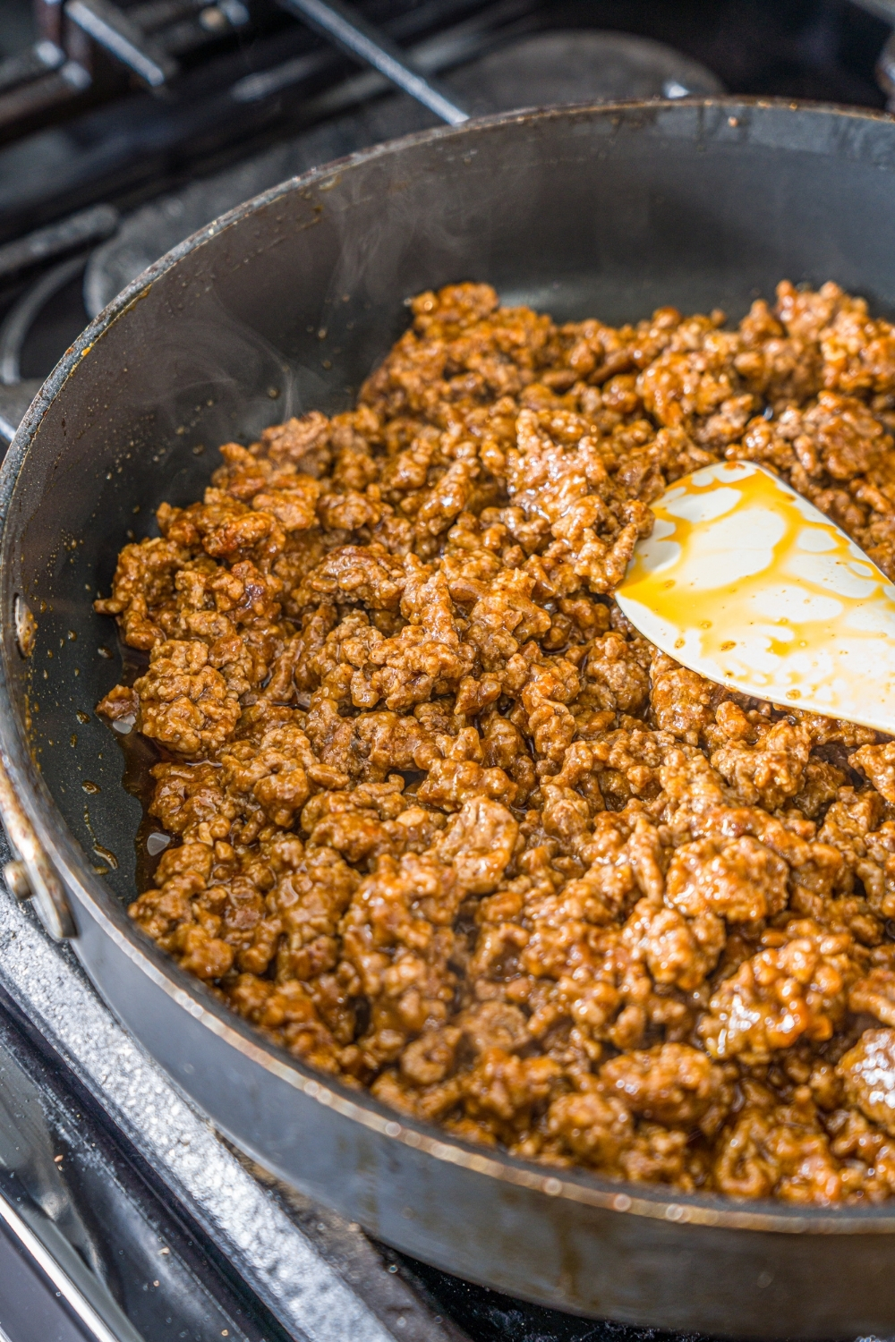 An oven with a skillet cooking taco meat. A spatula is mixing the beef and taco seasoning.
