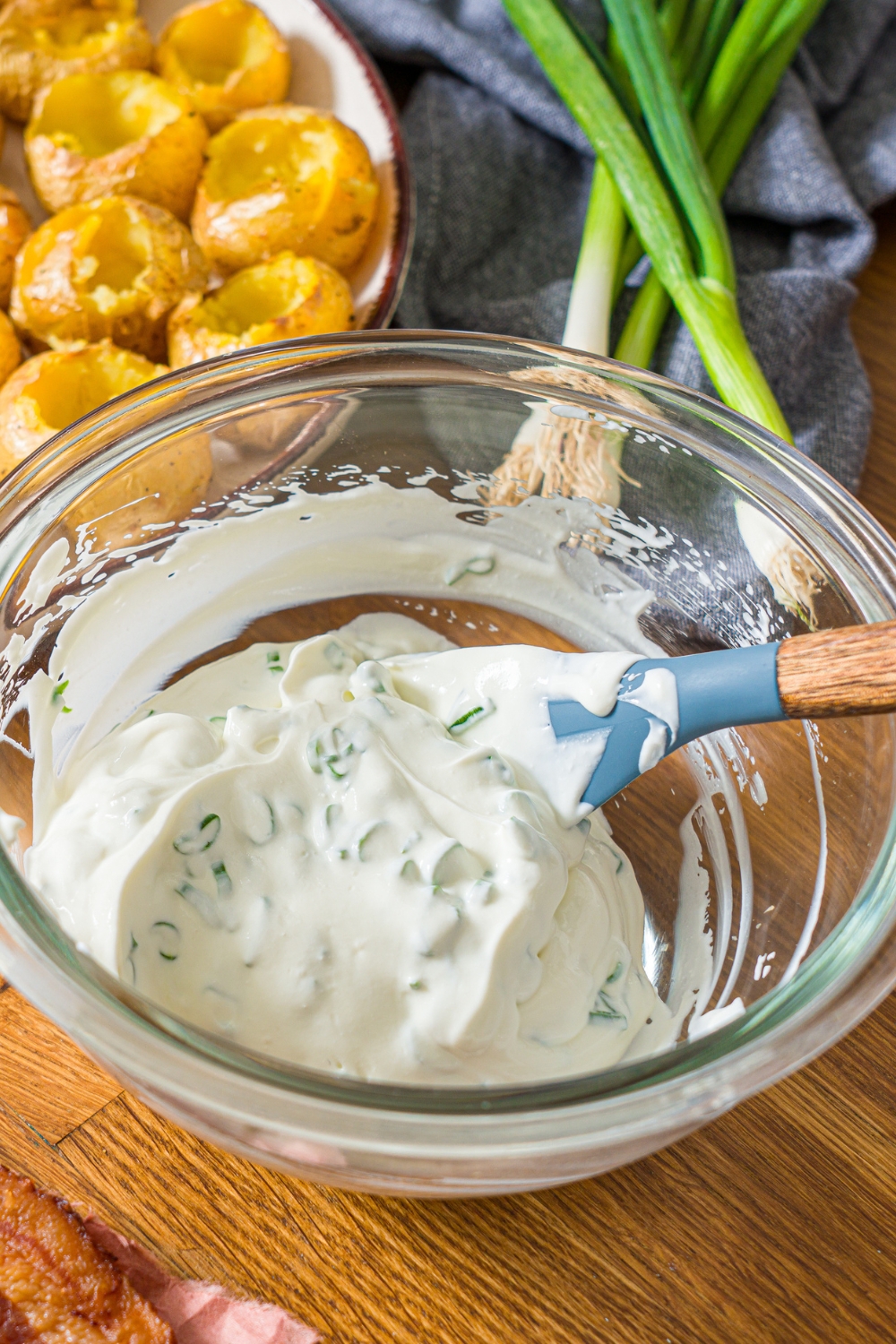 A glass bowl with a spatula mixing a sour cream mixture. The bowl is on a wooden counter.