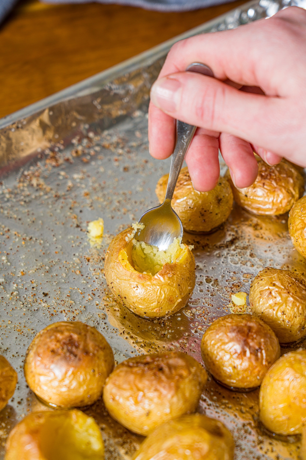 A baking sheet lined with foil with baked seasoned mini potatoes. There is a spoon scooping out one of the potatoes.