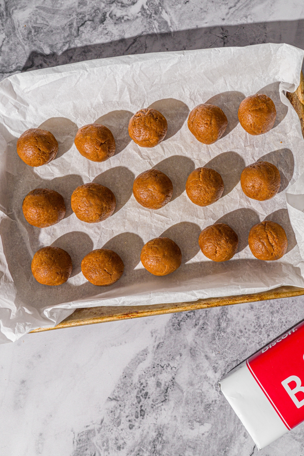 A baking sheet lined with parchment paper with Biscoff truffles. The sheet is on a marble counter.