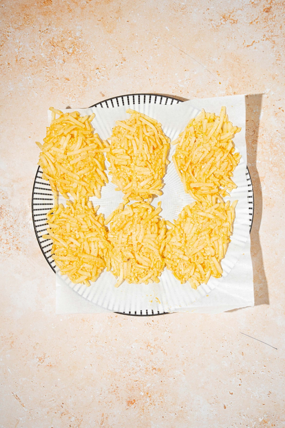 A plate lined with parchment paper with frozen parmesan hashbrowns. The plate is on a tan counter.