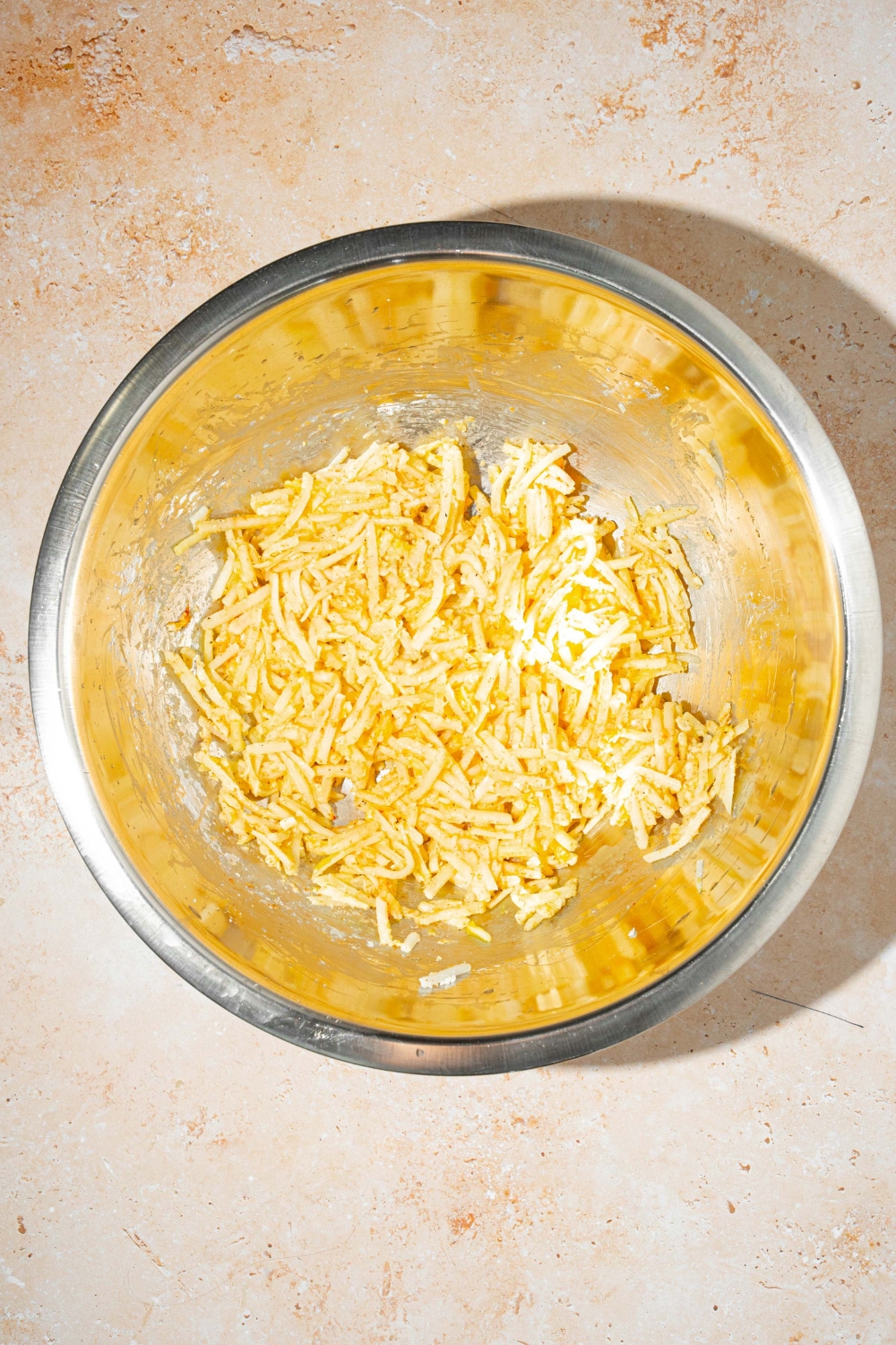 A bowl with a parmesan hashbrowns mixture. The bowl is on a tan counter.
