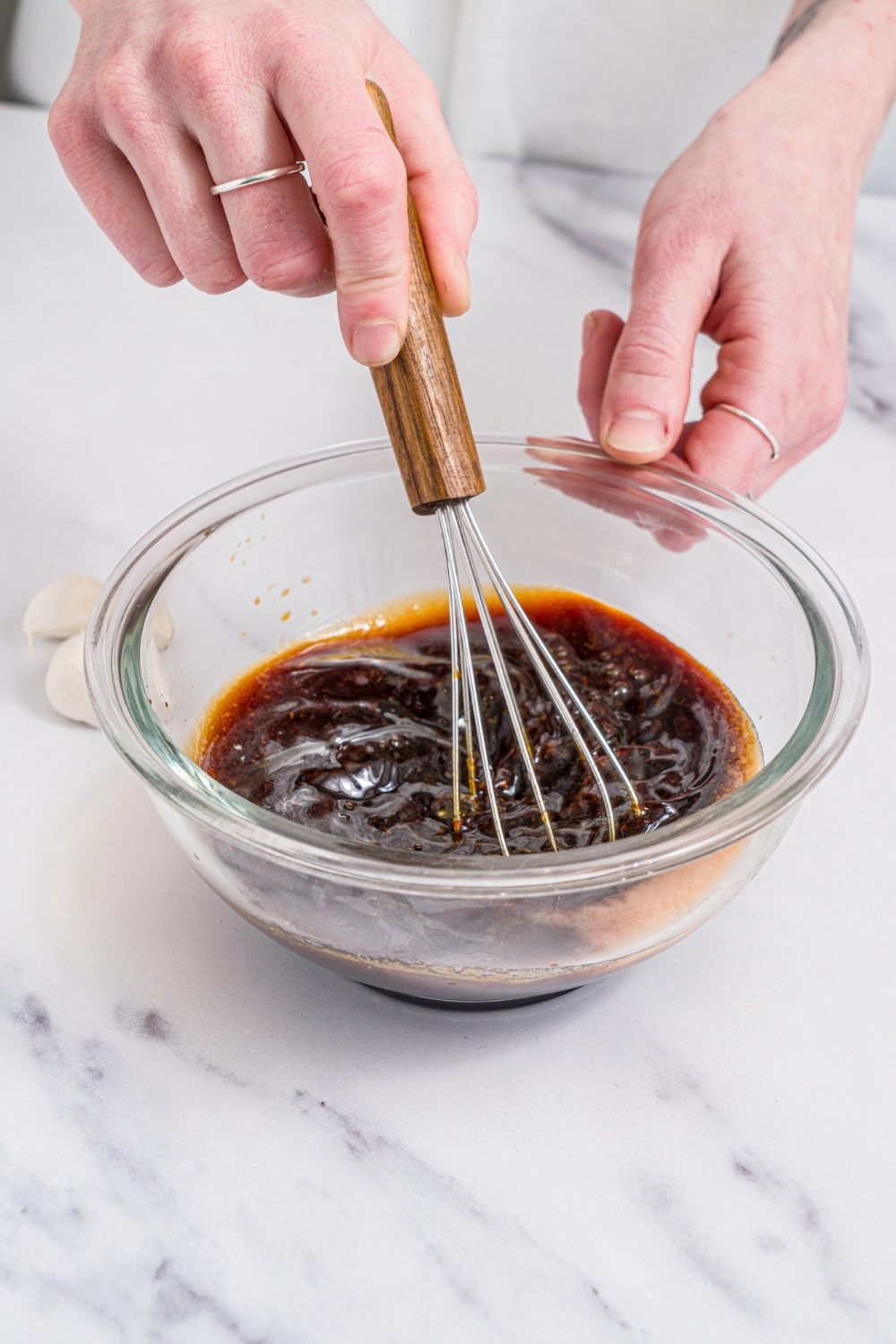 A glass bowl with a whisk mixing ingredients to make poke sauce. The bowl is on a marble coutner.