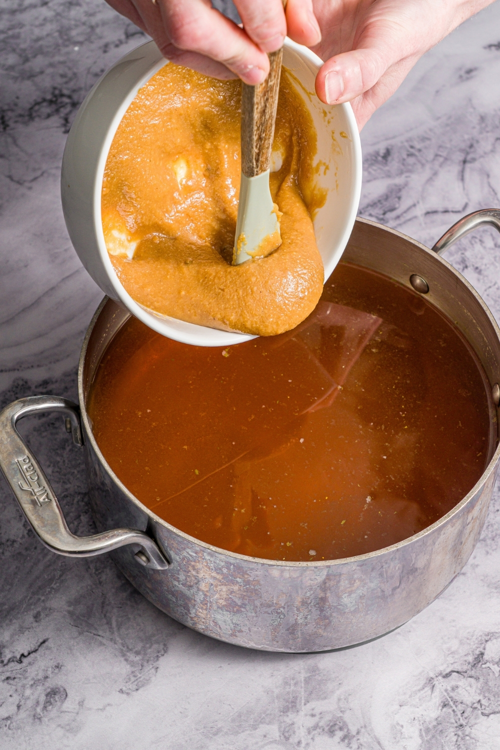 A large stock pot with pork broth. Miso slurry is being added to the broth. The pot is on a marble counter.