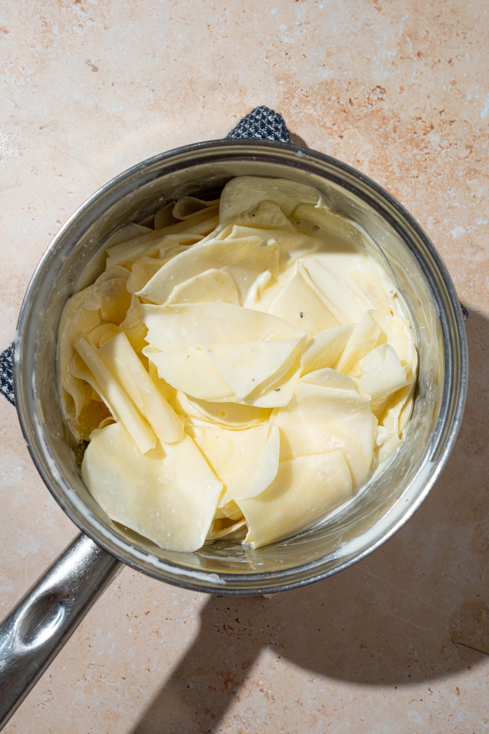 A pot with thinly sliced potatoes soaking in a cream sauce. The pot is on a tan counter.