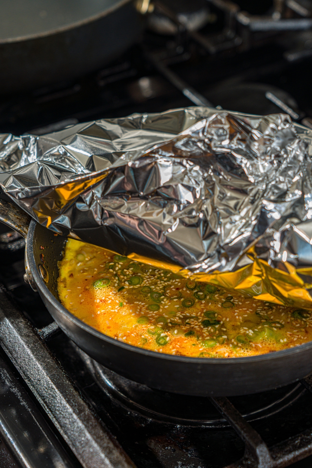 A skillet with a cooked egg and crispy rice mixture with foil being placed over the skillet.