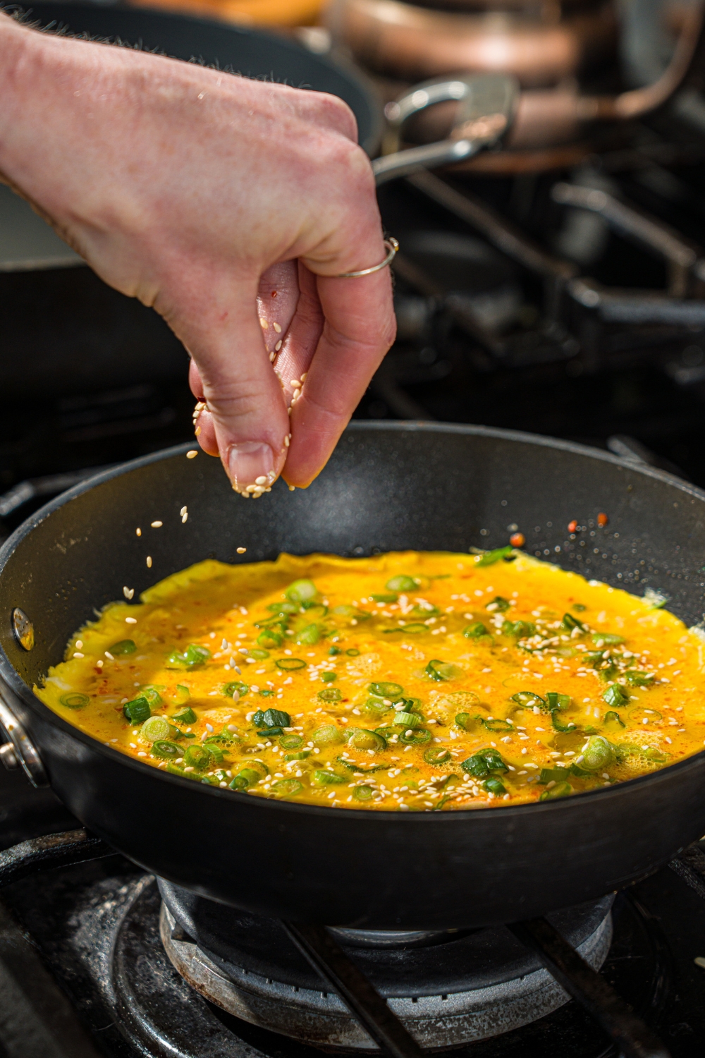 A skillet with a crispy rice and egg mixture. Sesame seeds are being added to the eggs.