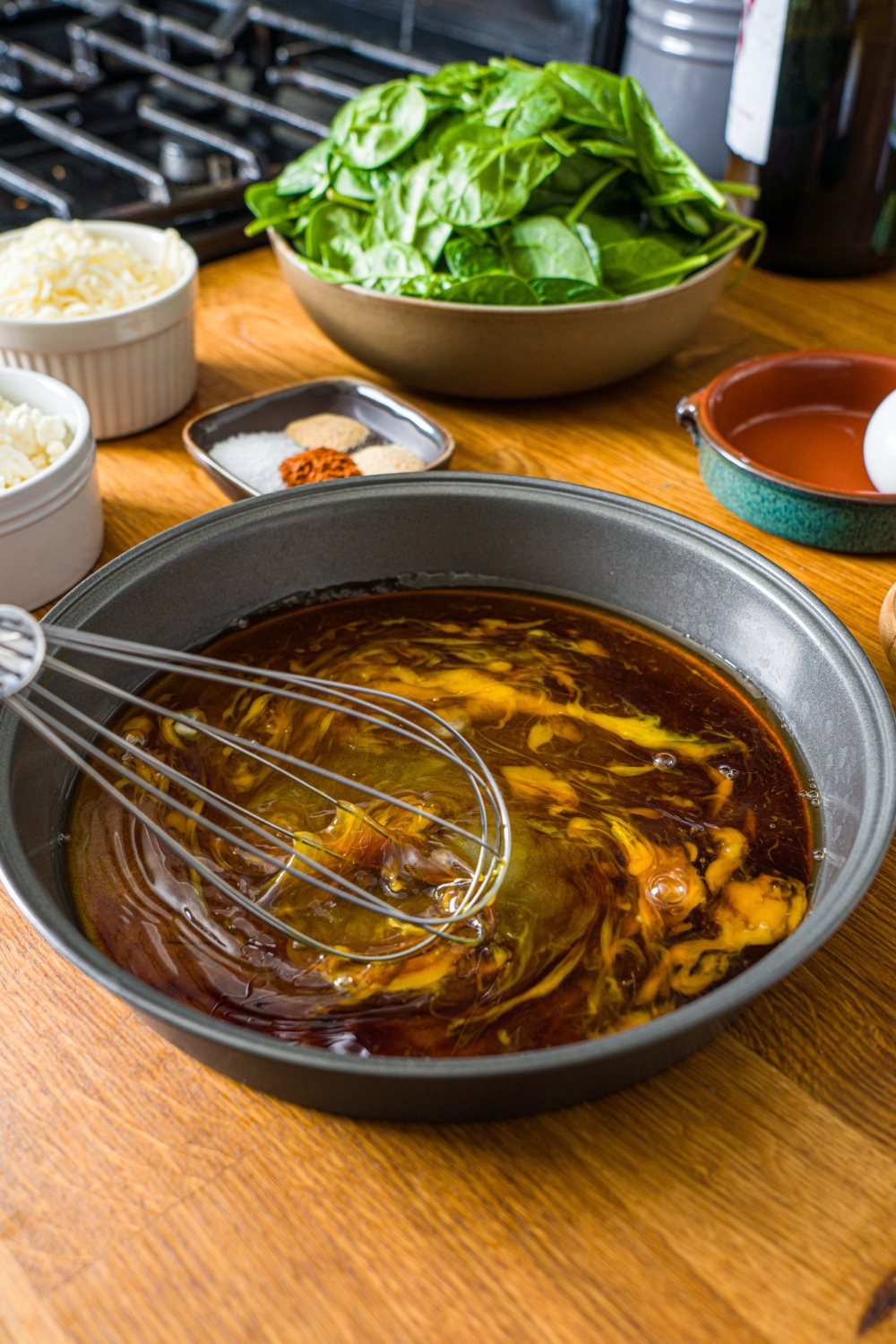 A tin with a whisk mixing an egg and soy sauce mixture. The tin is on a wooden counter.