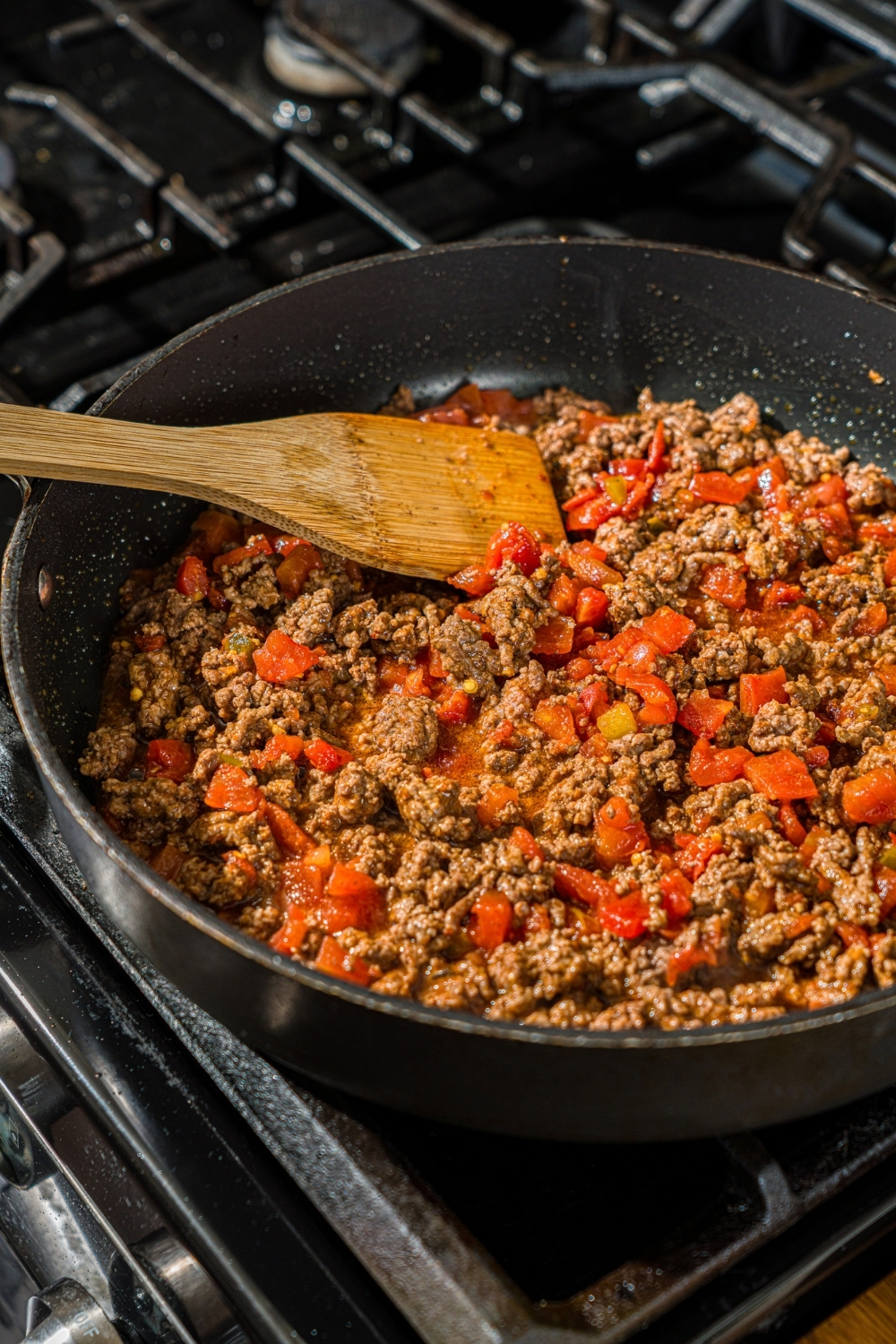 A skillet with a wooden spoon mixing a seasoned ground beef and Rotel mixture.
