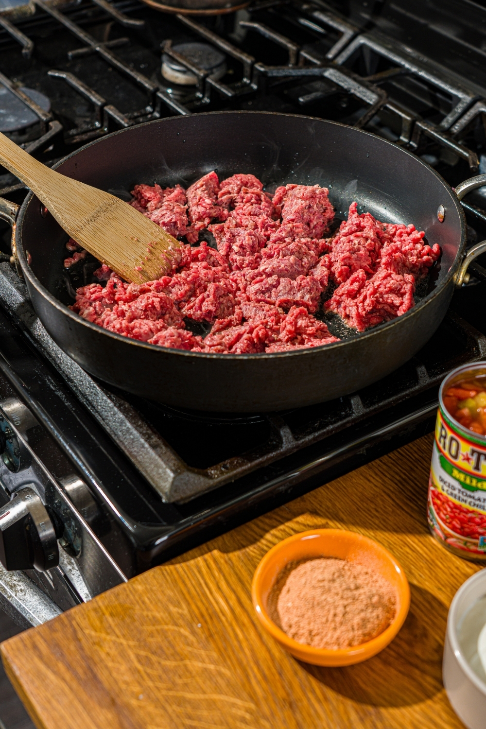 A skillet with a wooden spoon breaking up ground beef as it cooks.