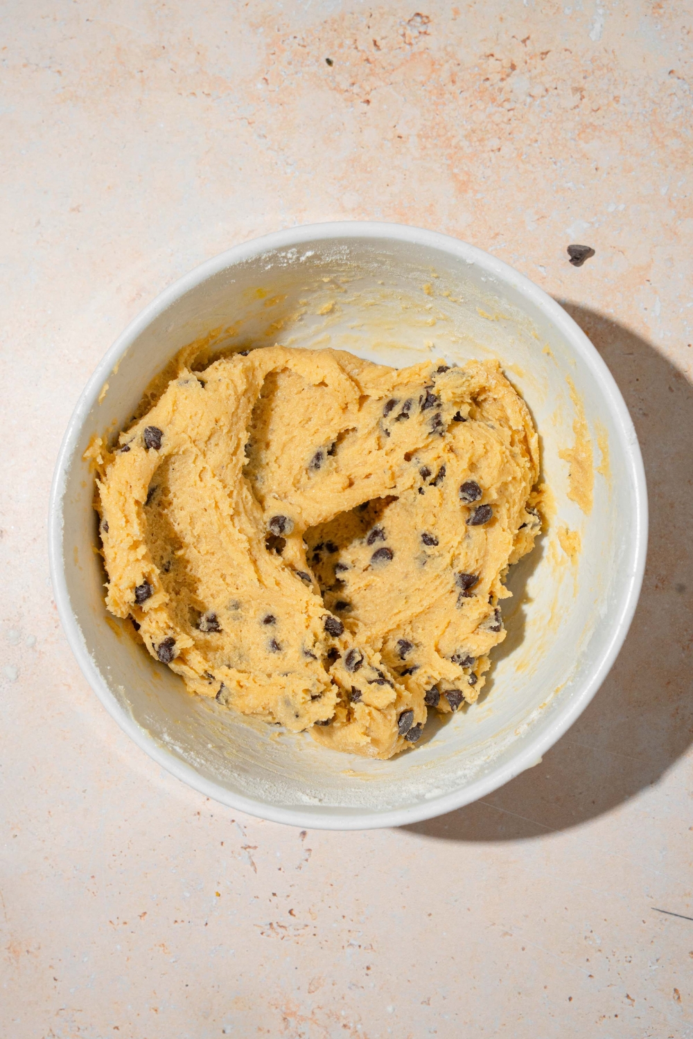 A large white bowl with chocolate chip cookie dough. The bowl is on a tan counter.