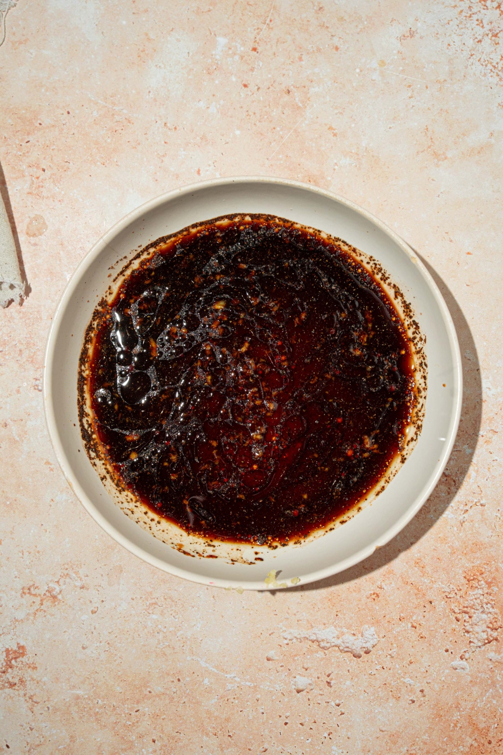 A white plate with skirt steak marinade with soy sauce, balsamic vinegar, garlic, salt and pepper, and oil. The plate is on a tan counter.
