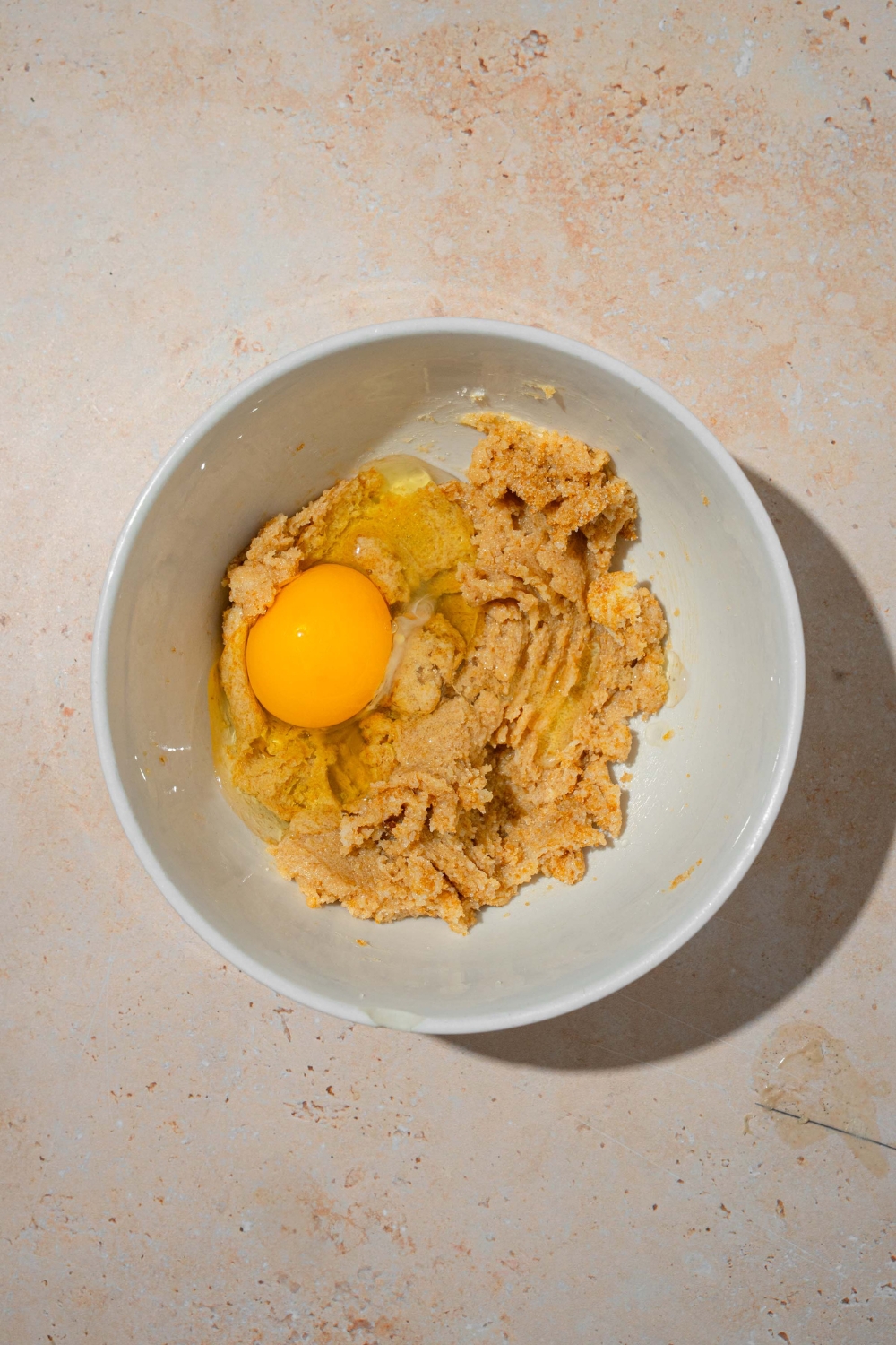 A white bowl with creamed sugar and butter with egg. The bowl is on a tan counter.