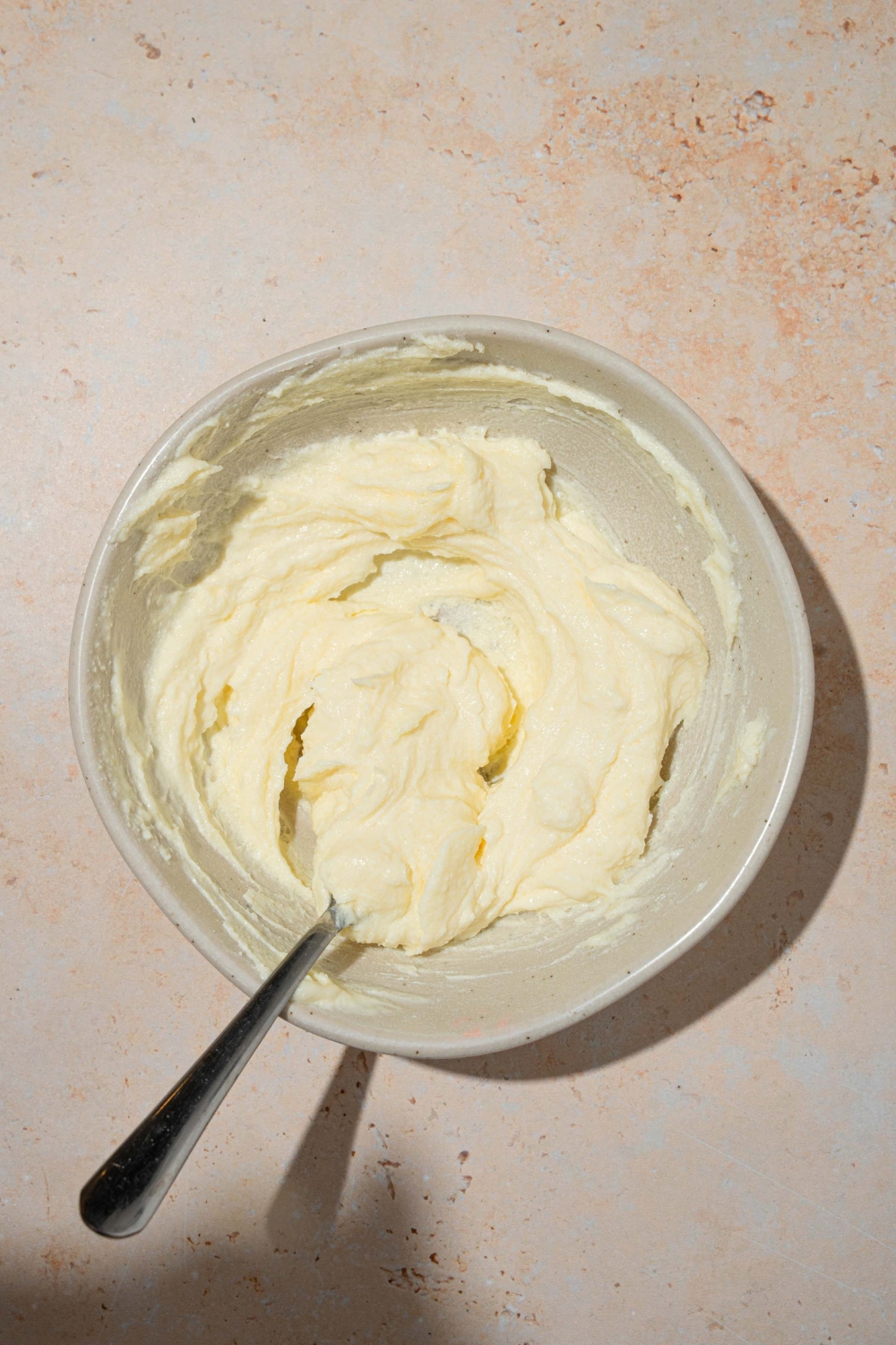 A large white bowl with a spoon mixing a cream cheese and sugar filling. The bowl is on a tan counter.