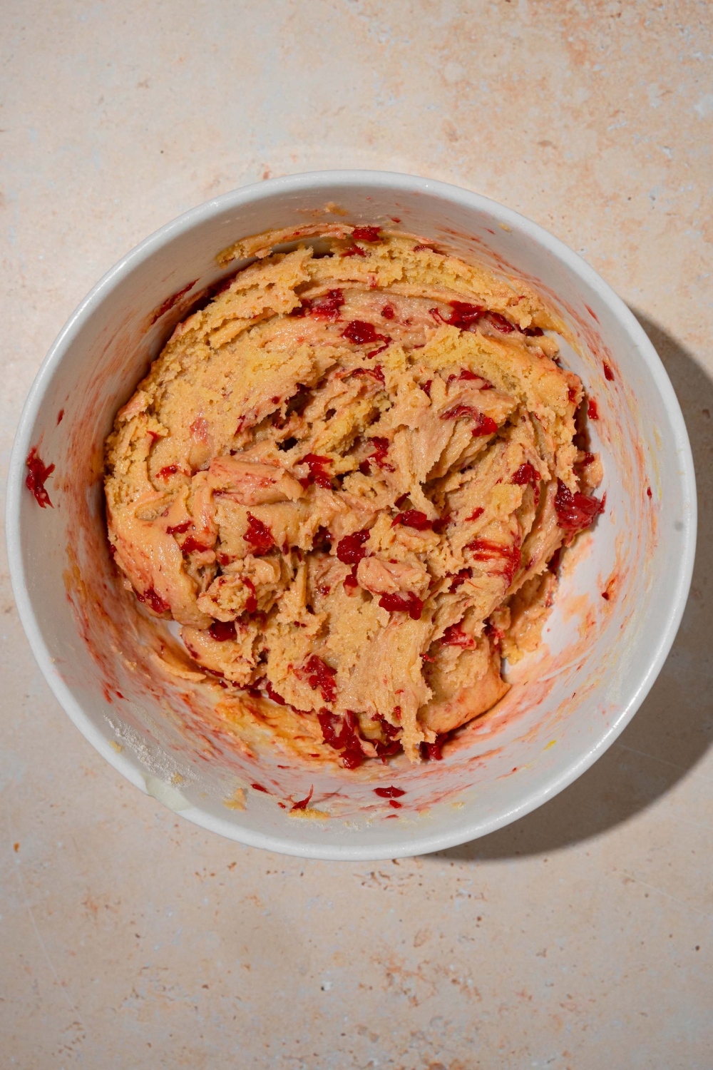 A large white bowl with cookie dough mixed with strawberry jam. The bowl is on a tan counter.
