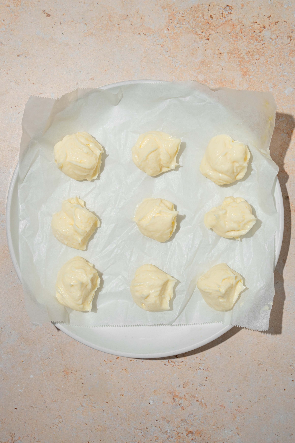 A white plate lined with parchment paper with several scoops of cheesecake filling. The plate is on a tan counter.