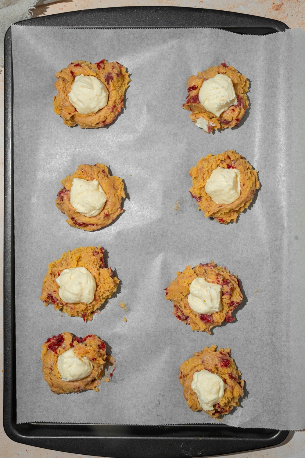 A baking sheet lined with parchment paper with unbaked strawberry cheesecake cookies.