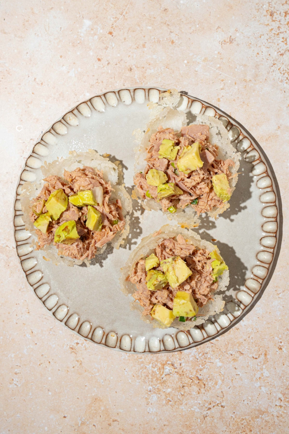 A plate with three tuna cups topped with avocado. The plate is on a tan counter.