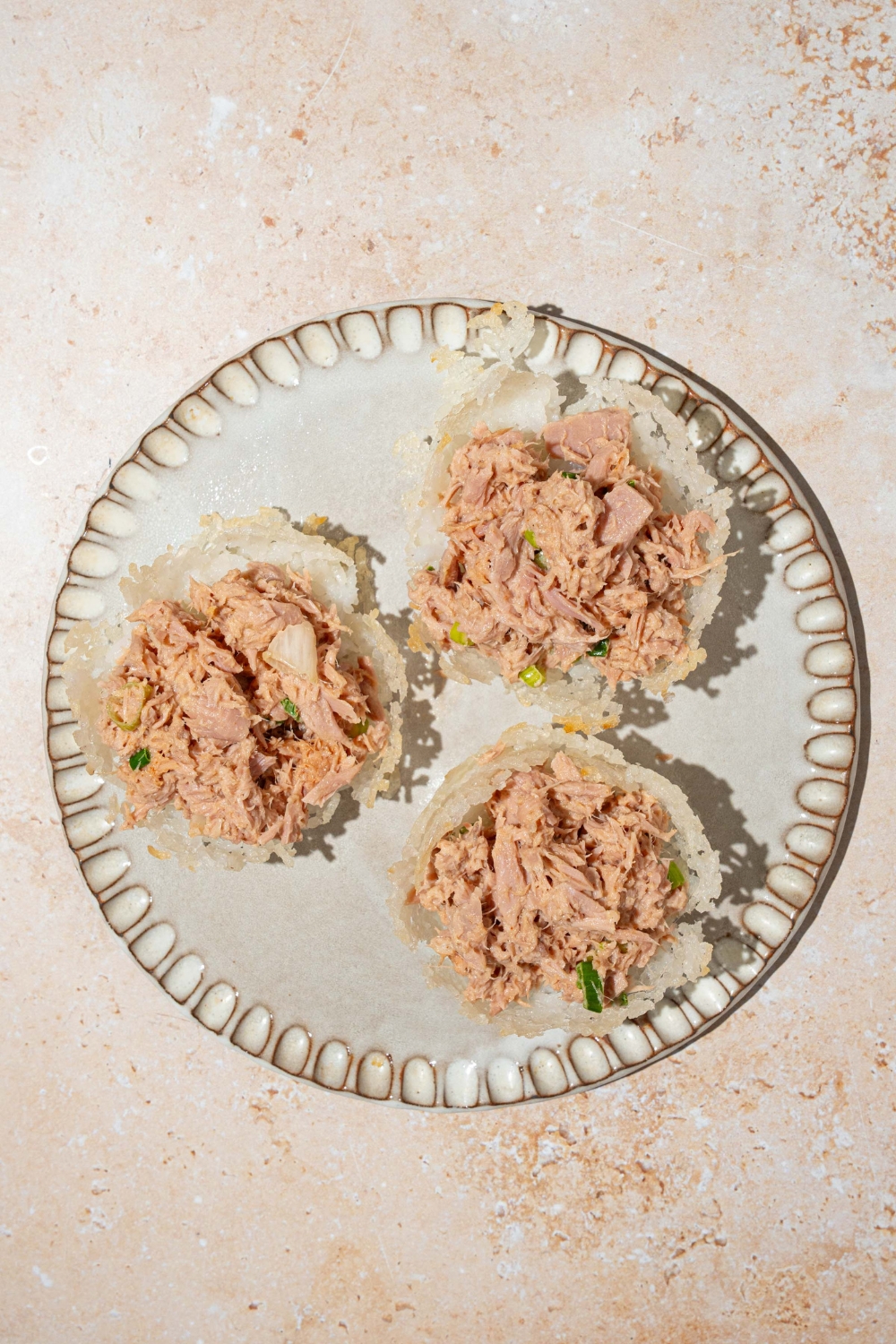 A plate with three rice cups filled with tuna salad. The plate is on a tan counter.