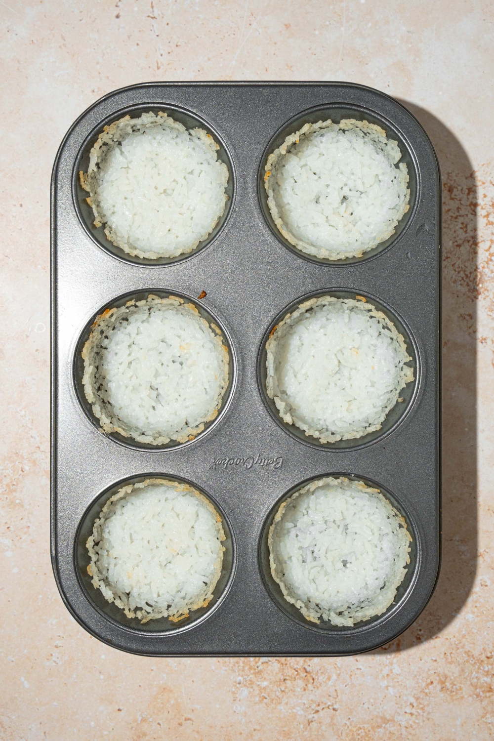 A muffin pan with cooked rice shaped in each. The pan is on a tan counter.